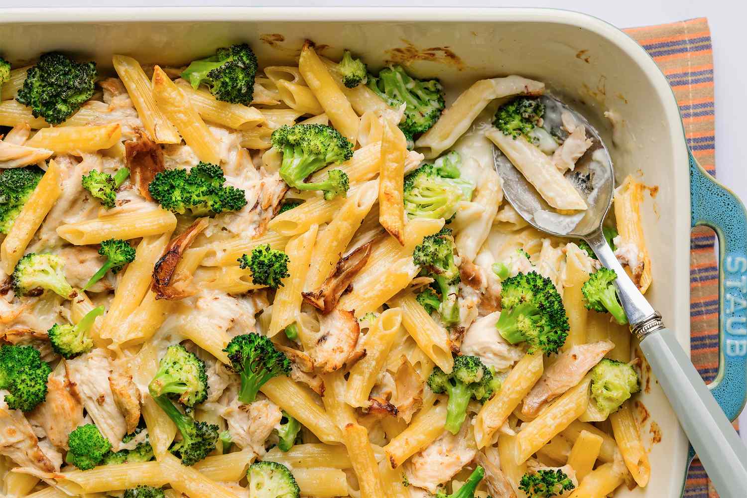 Baked chicken Alfredo pasta with broccoli in a casserole dish with a spoon