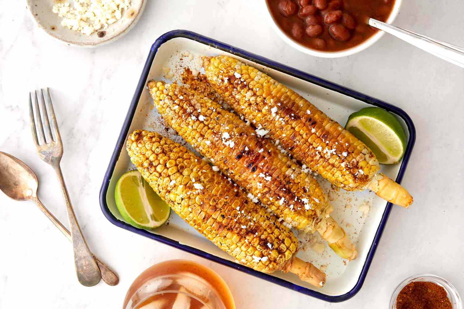 Cajun-Spiced Grilled Corn in a Casserole Dish with Two Lime Halves, Surrounded by a Table Setting