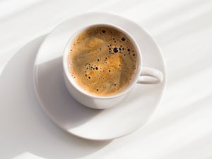 Overhead view of a cup of coffee and a white saucer on a white background