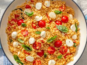 Dish featuring cooked orzo pasta with cherry tomatoes mozzarella and basil garnished on top