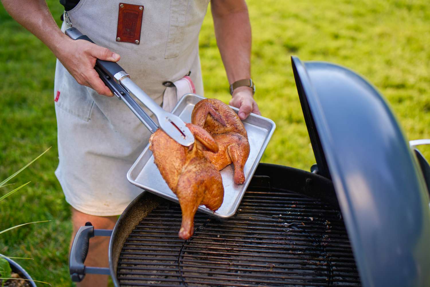 Person grilling a spatchcocked chicken on a barbecue with tongs