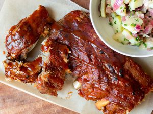 bbq ribs on a plate next to a bowl of potato salad 