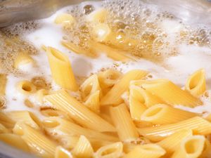 Penne pasta boiling in water with foam at the surface in a pot