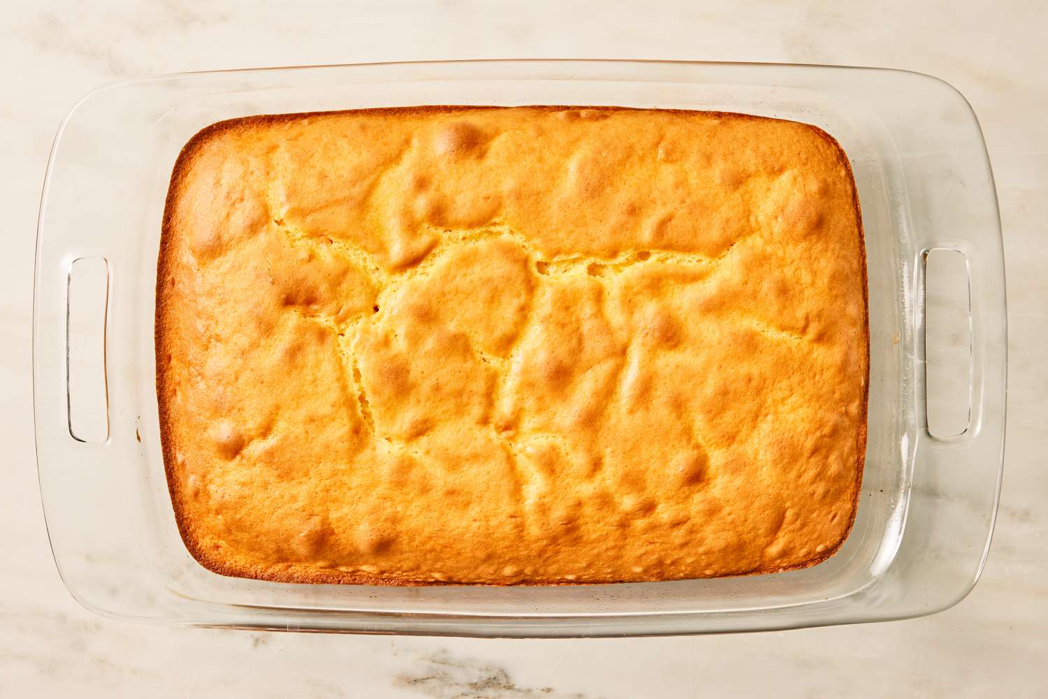 Overhead view of a glass baking dish with the baked cake layer before adding frosting for Pig Pickin' Cake recipe