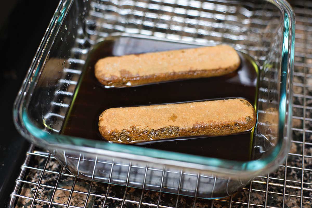 A glass dish of espresso syrup with two ladyfingers soaking in it