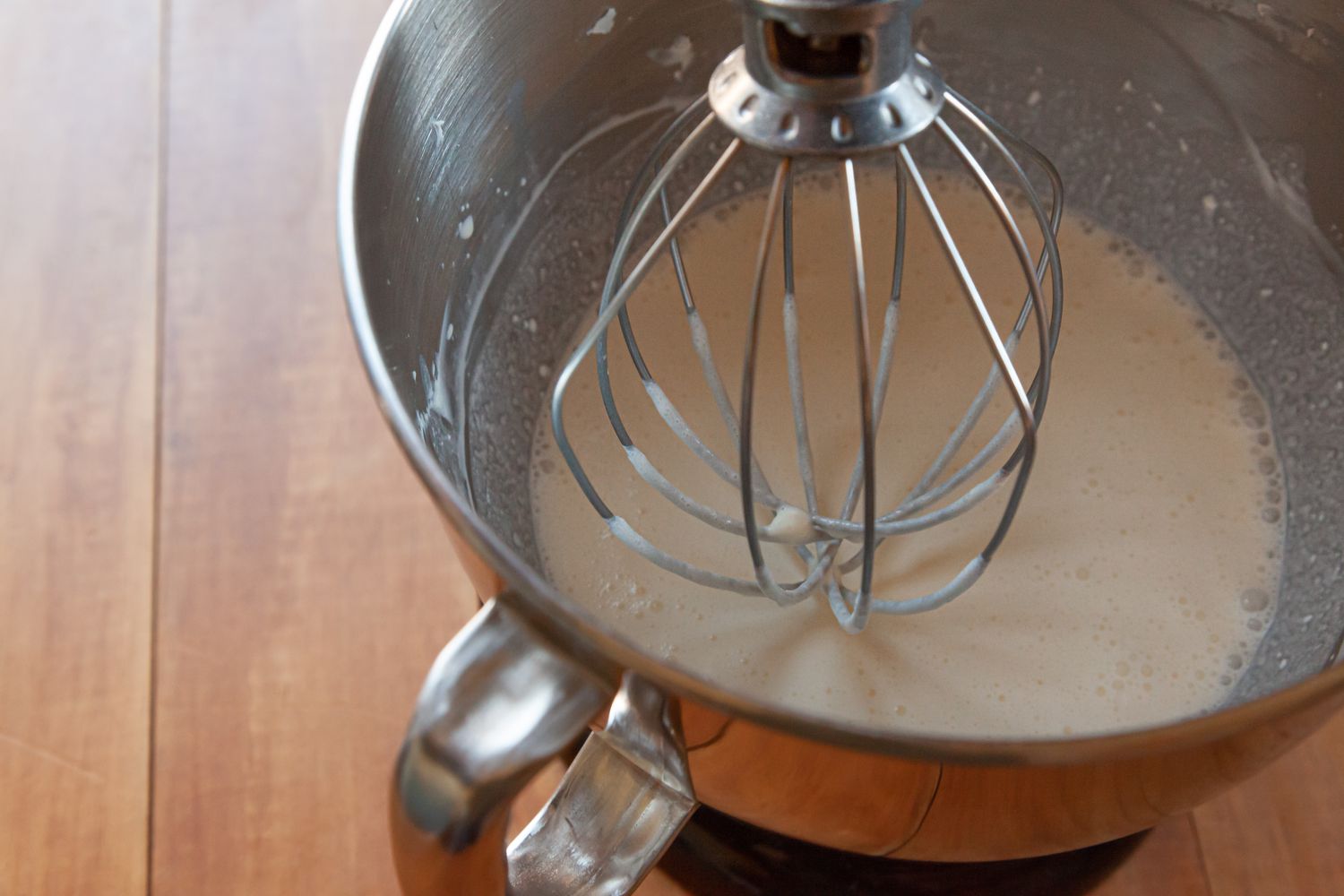 Overhead view of a stand mixer with a whisk attachment making a whipped cream frosting with cream cheese.