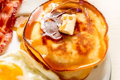 A plate with pancakes topped with butter and syrup served alongside bacon and a fried egg