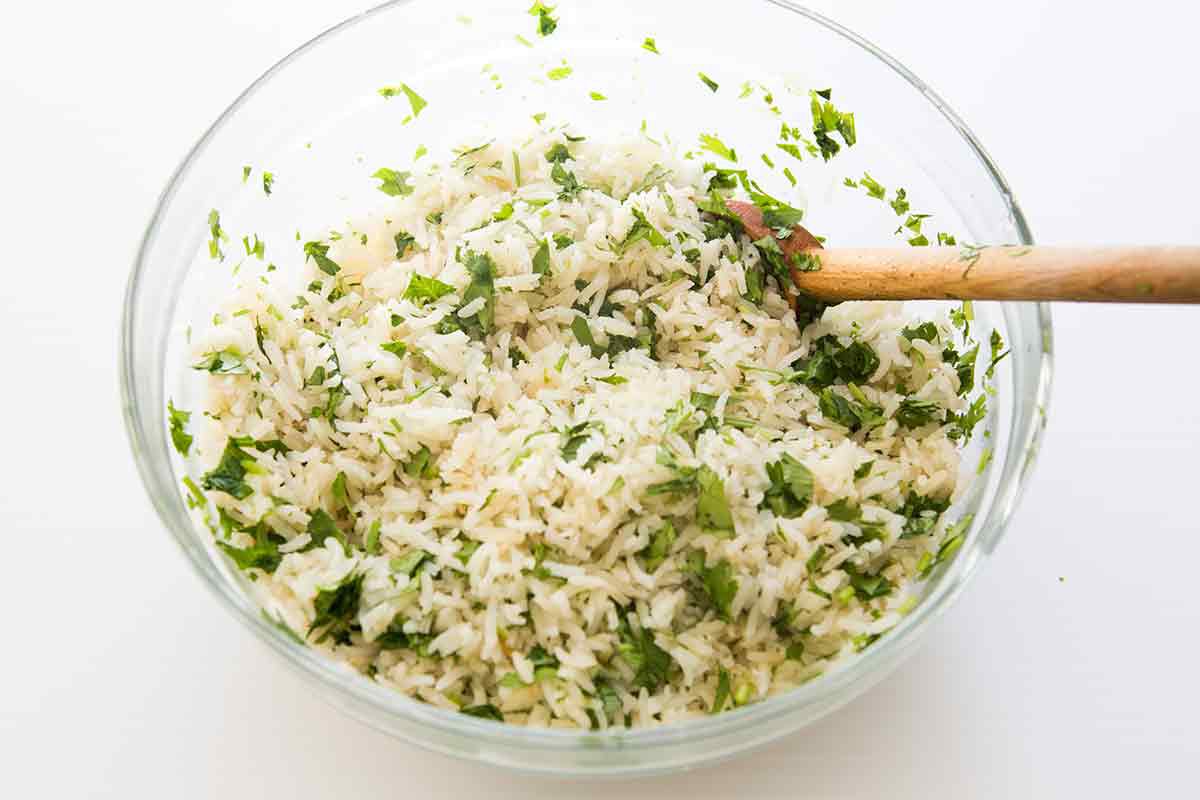 Lime juice and cilantro being mixed in a glass bowl with a wooden spoon