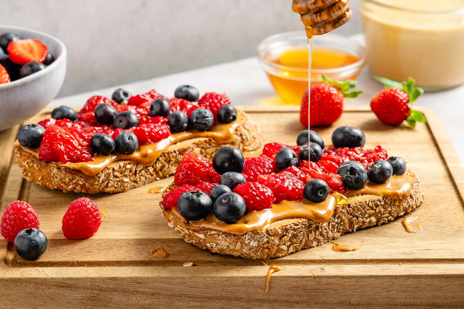 Peanut butter toasts topped with raspberries, blueberries, and a drizzle of honey