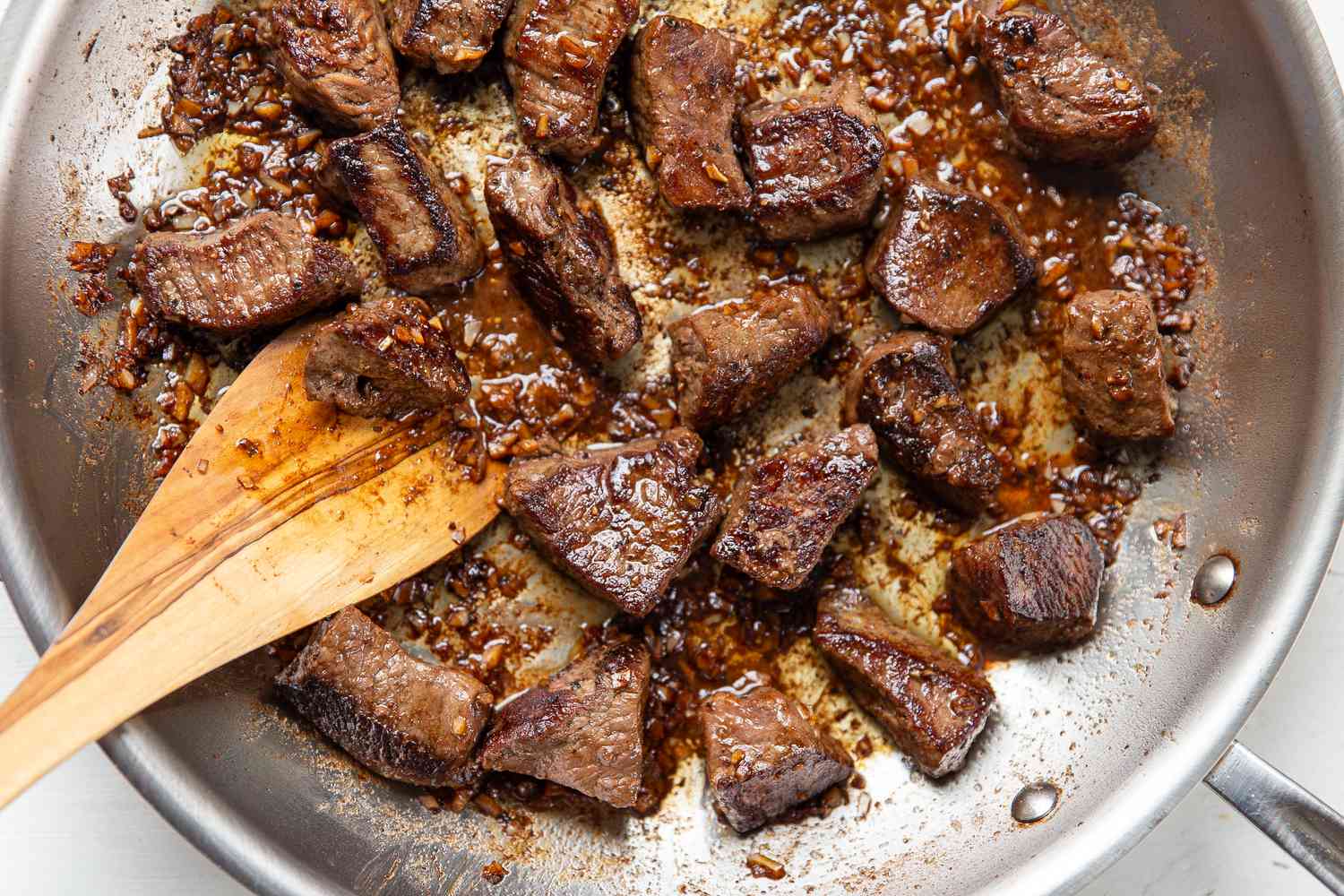 Overhead view of a stainless steel skillet of Garlic Butter Steak Bites with a wooden spatula