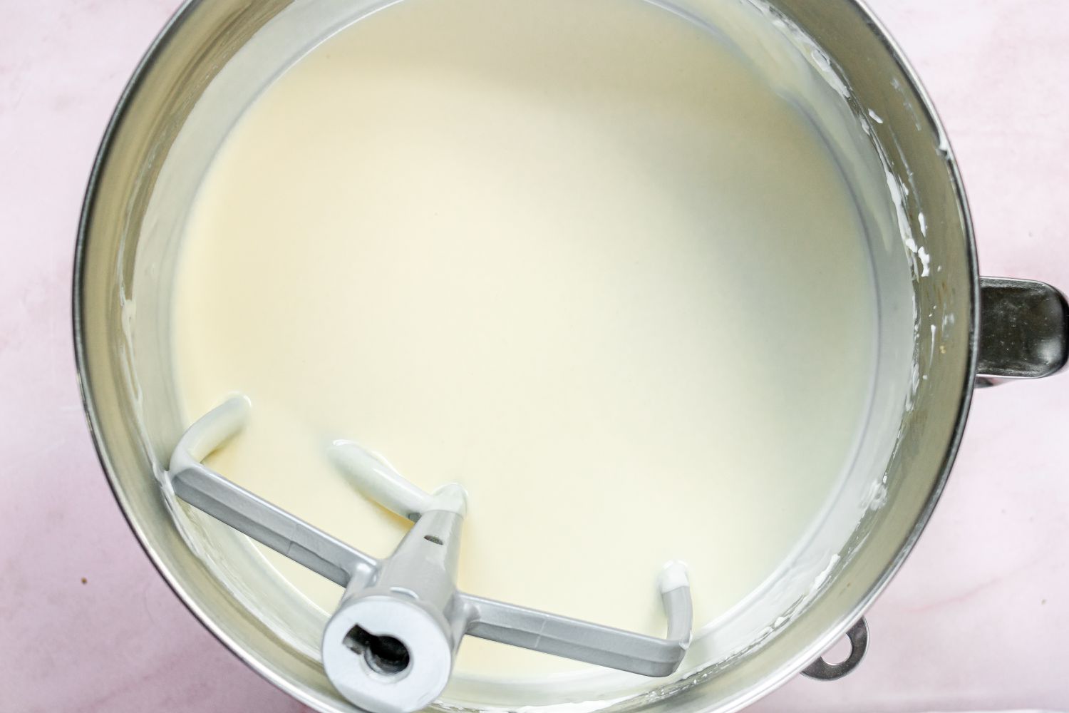 Heavy cream being added to the cheesecake mixture in a stand mixer