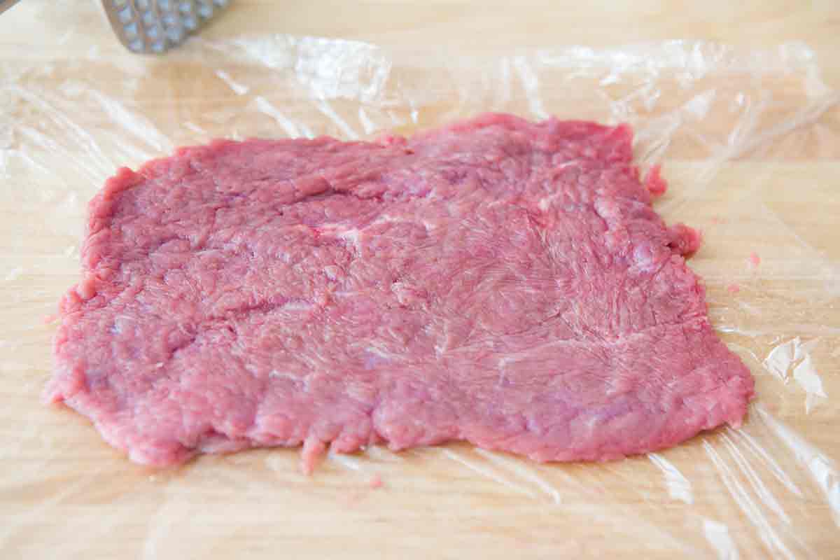 Thin beef for country fried sirloin on a sheet of plastic wrap