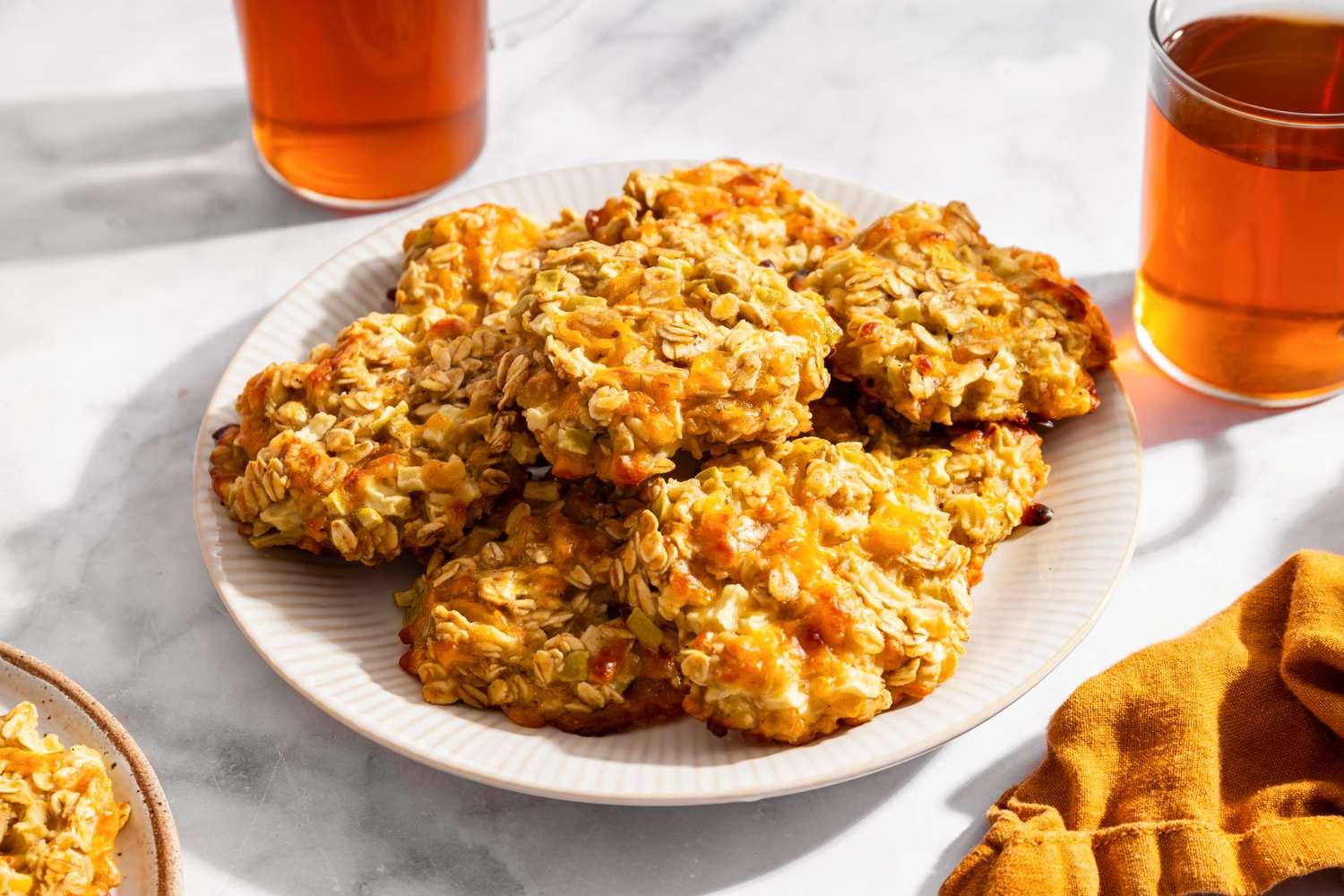 Plate of oat cookies with apple and cheddar accompanied by glasses of a beverage and a cloth napkin