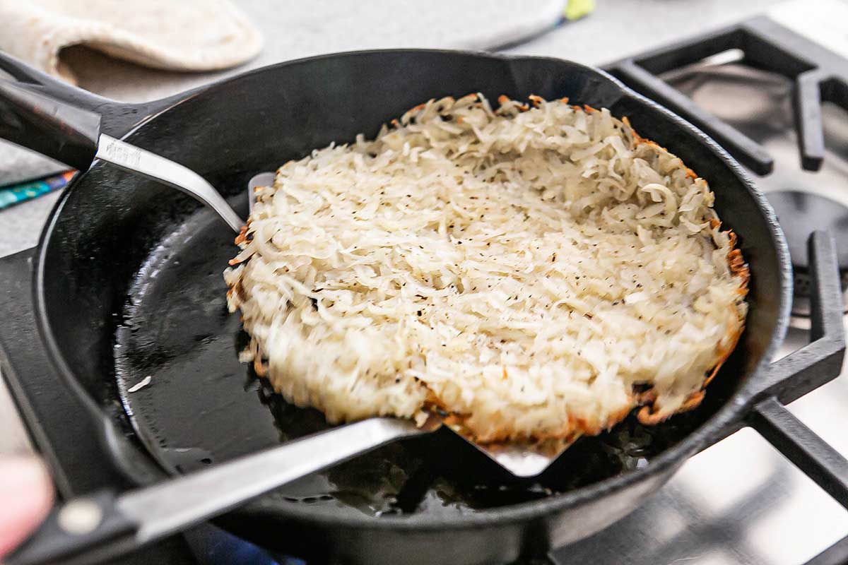 Hash browns being flipped with spatulas in a cast iron skillet