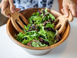 Mixed slad greens getting tossed together in a wooden bowl