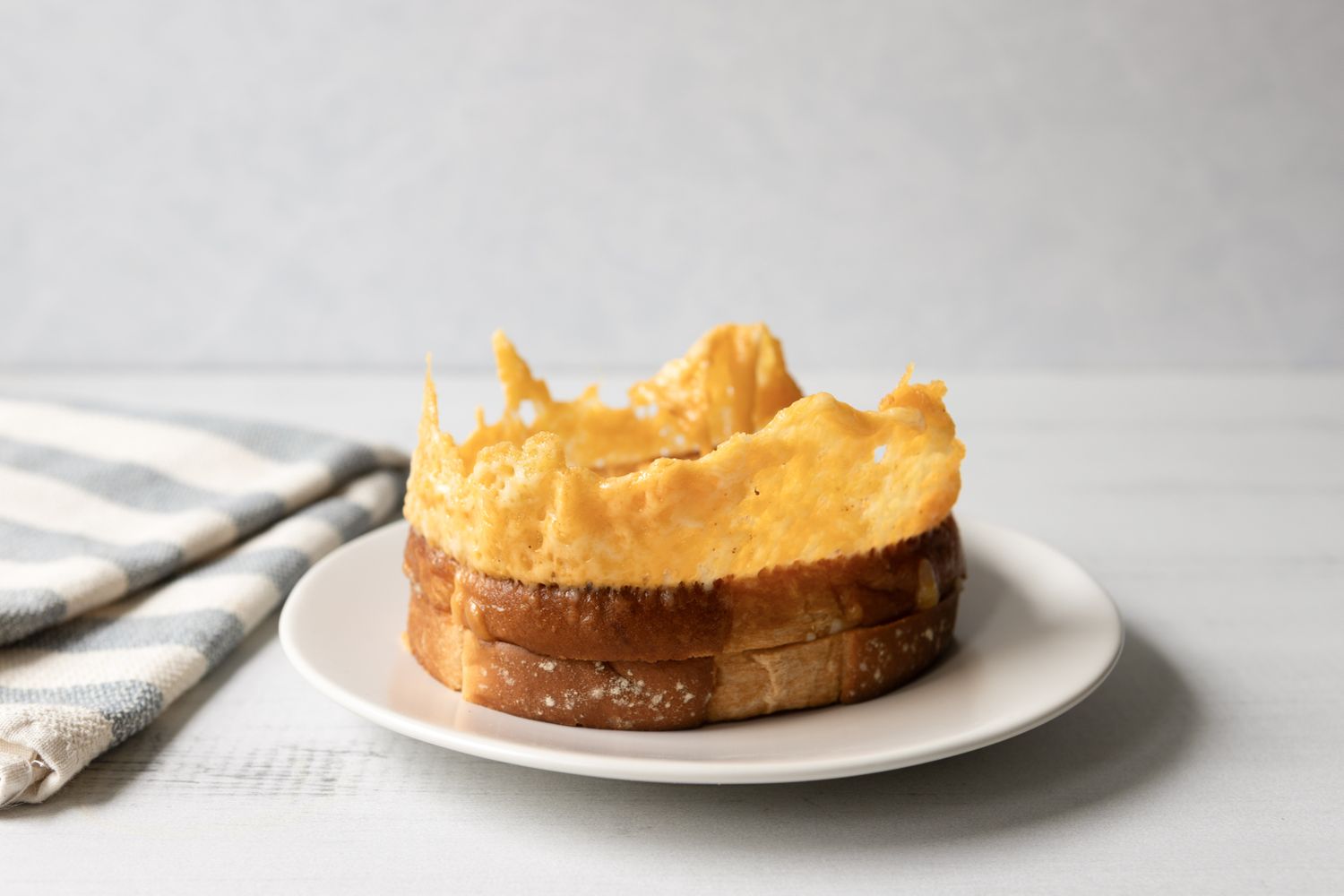 A grilled cheese sandwich served on a white plate part of the bread appears hollowed out and crispy melted cheese is visible