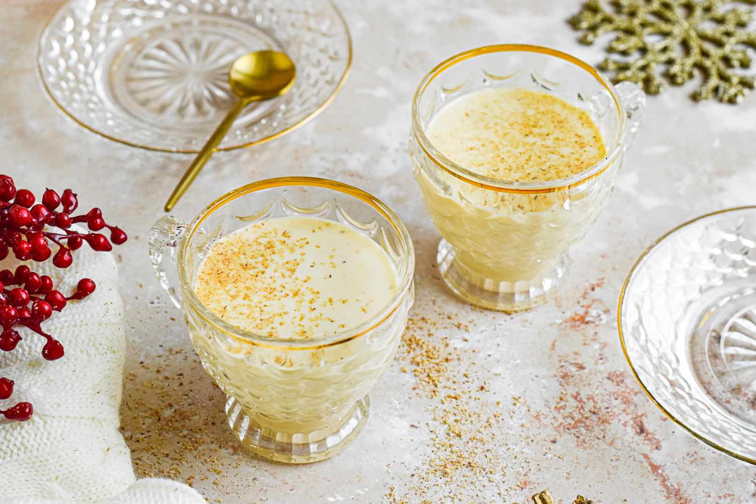 Two gold-rimmed glasses of eggnog cocktail that are dusted with cinnamon 
