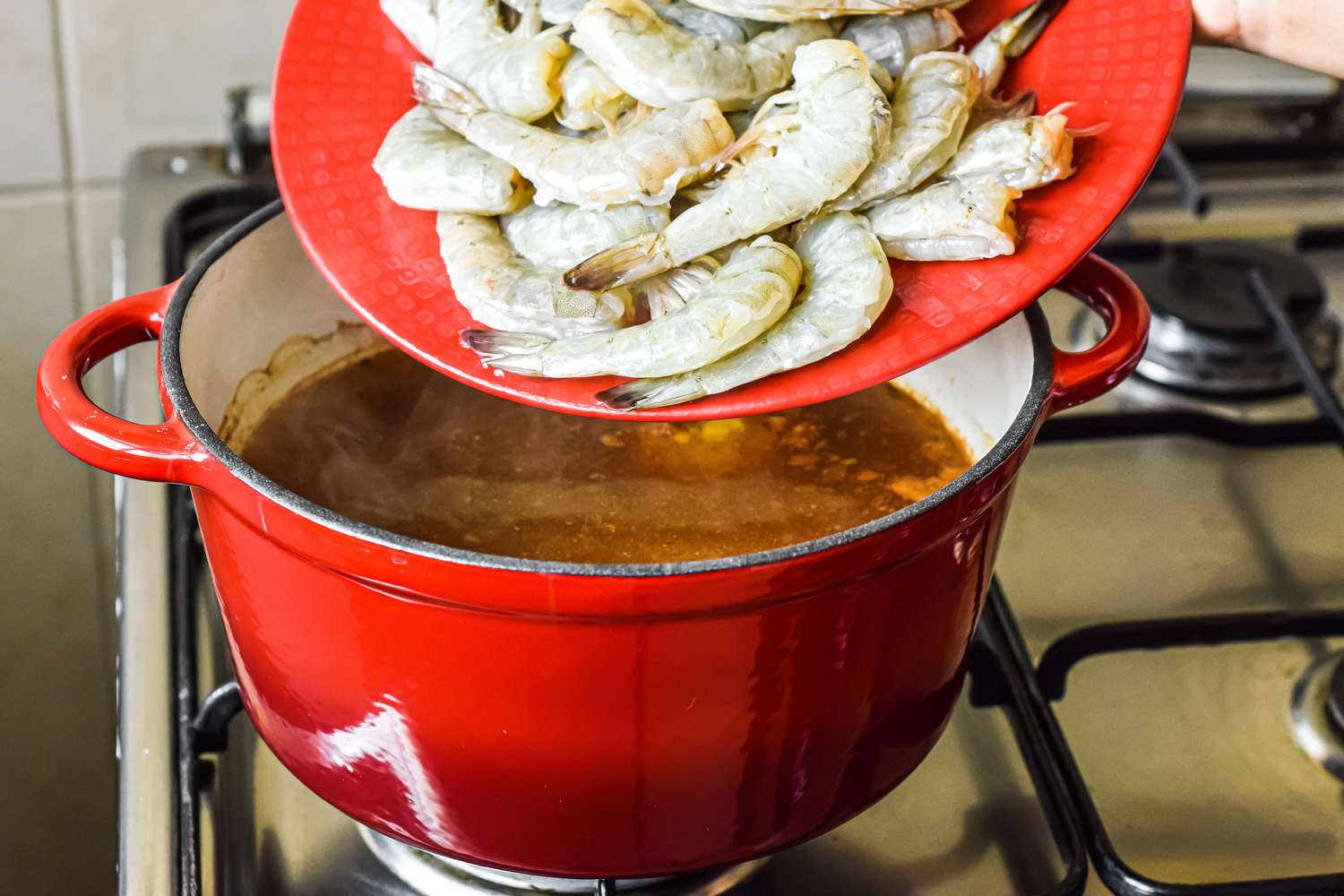 Adding raw shrimp to a pot of seasoned water for boiling for a shrimp cocktail recipe