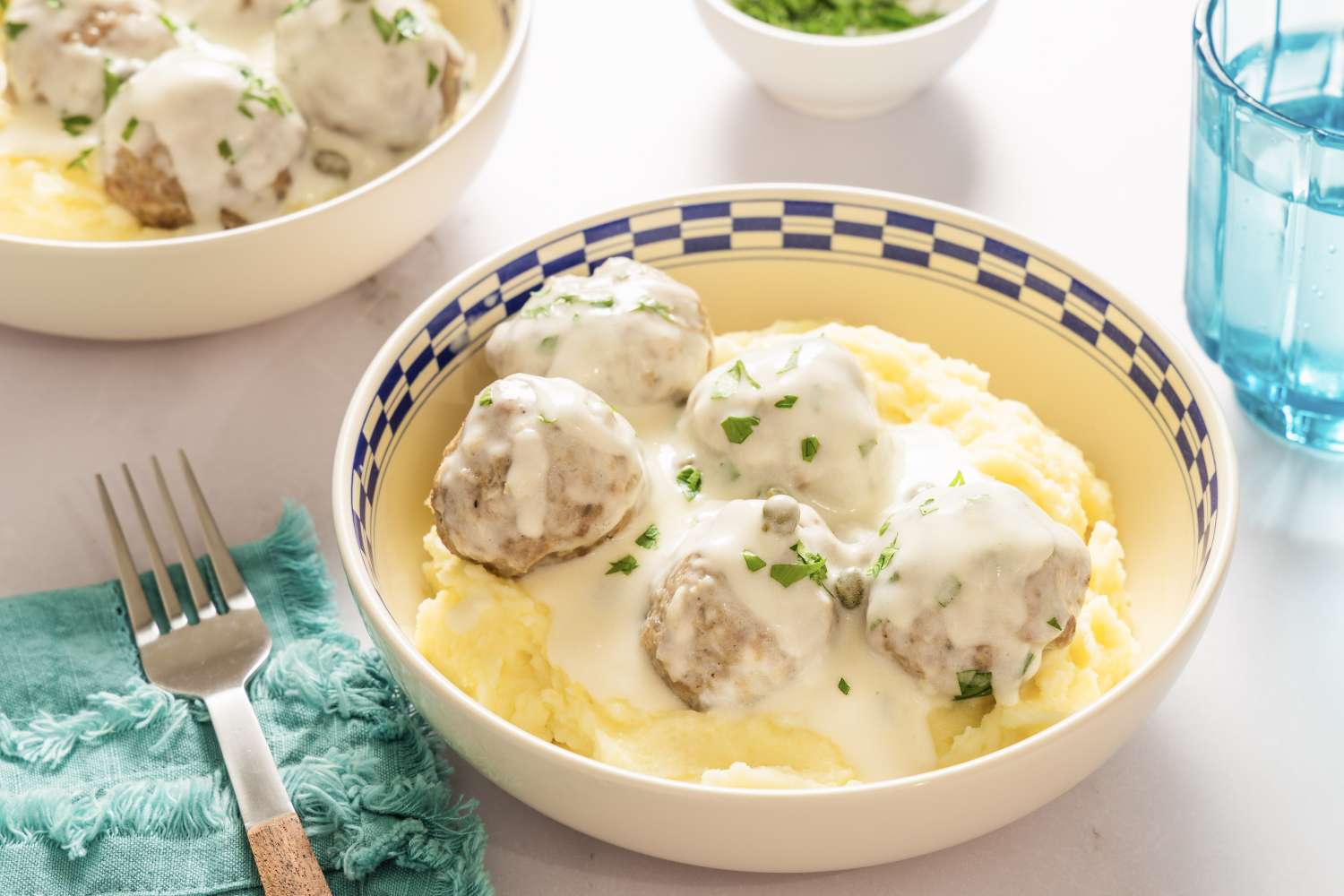 A bowl of Konigsberger Klopse with mashed potatoes garnished with chopped parsley