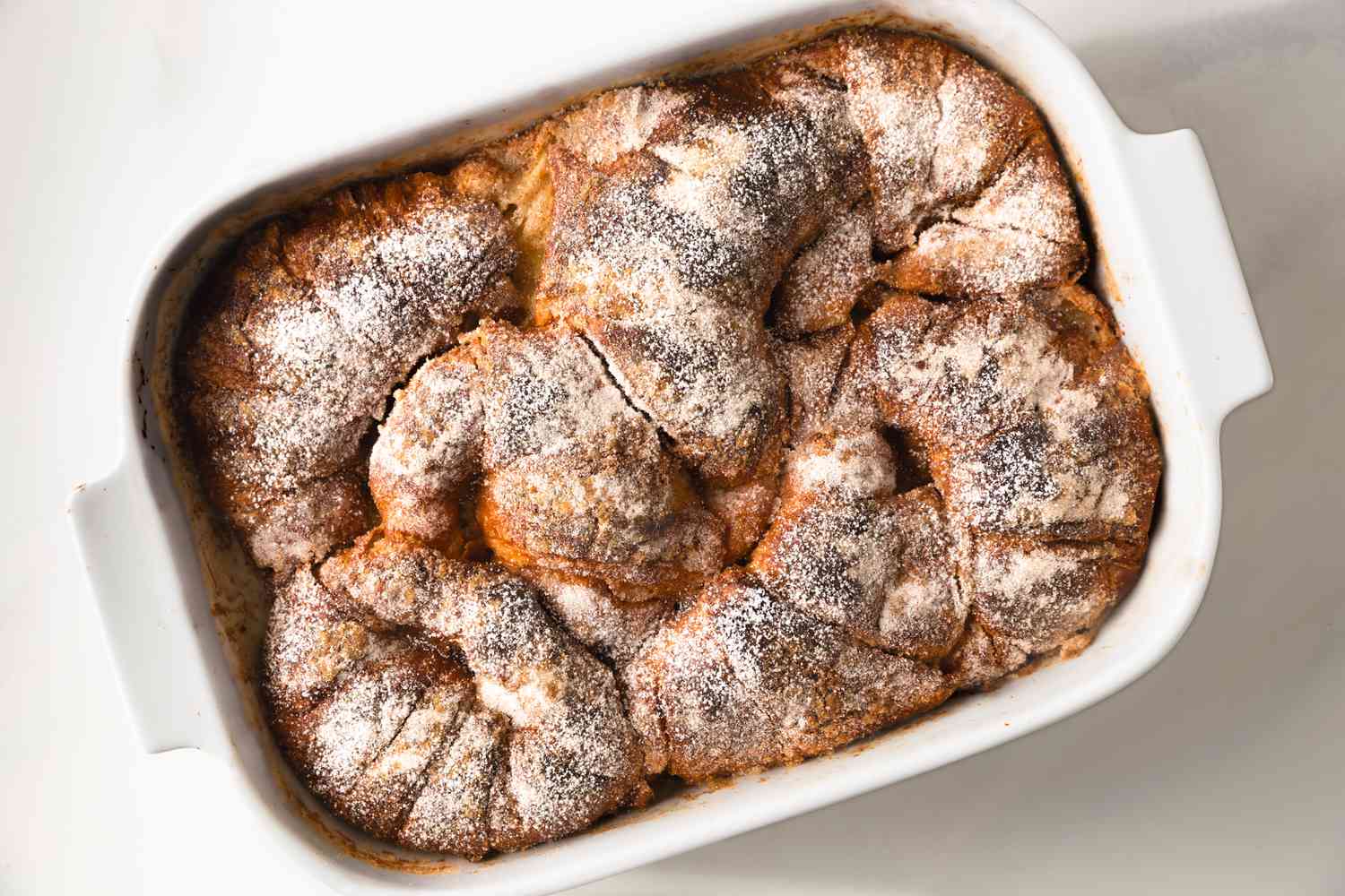 Overhead view of a white baking dish of Croissant French Toast casserole on a white countertop