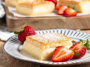 A serving of the magic cake recipe on a plate, with fresh strawberries around it for garnish