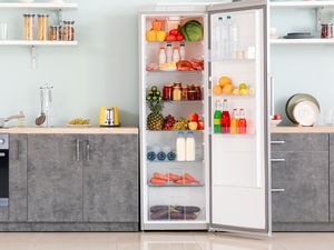 Open refrigerator in a modern kitchen, shelves filled with food and beverages