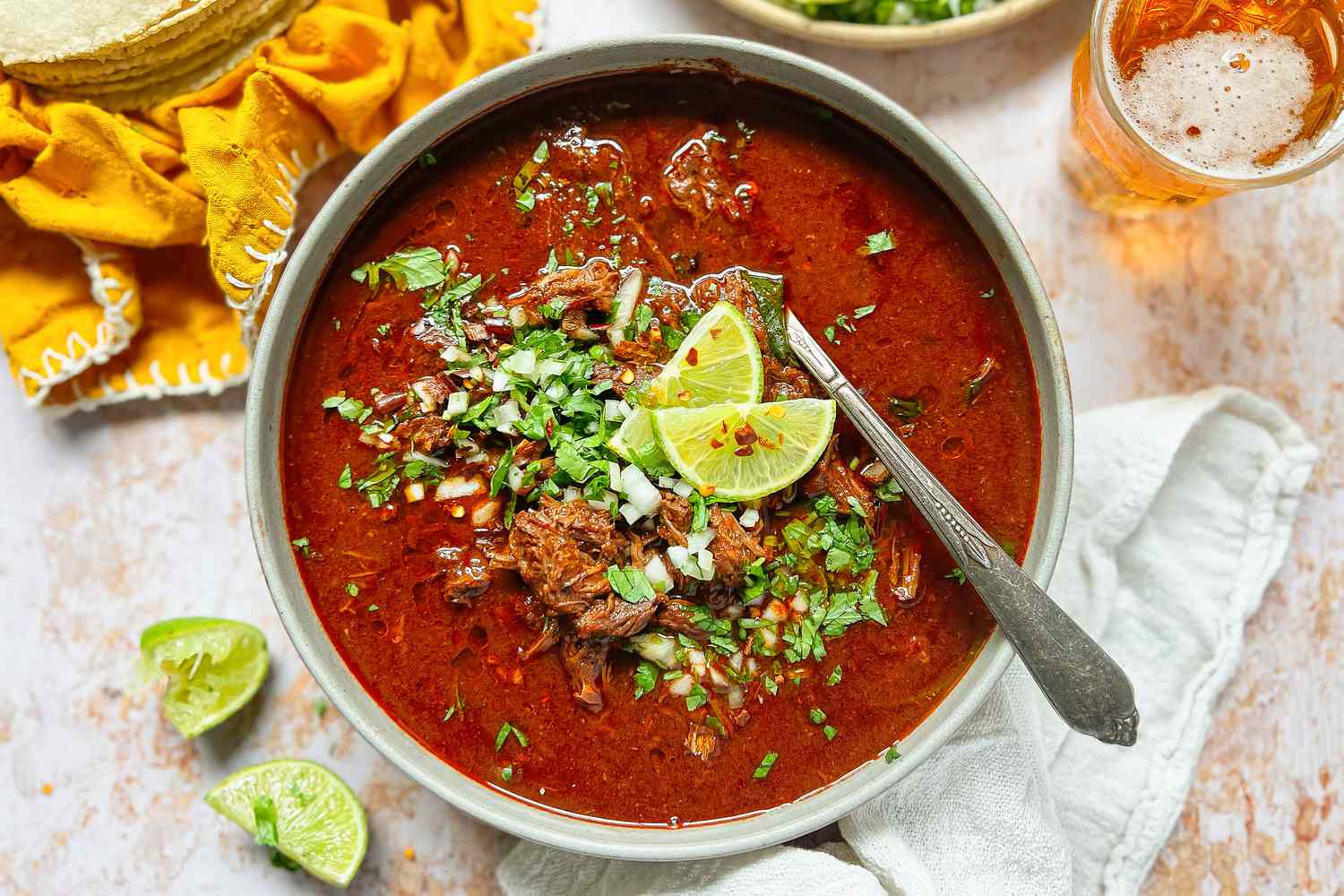 Deep red bowl of beef Birria with all the fixings