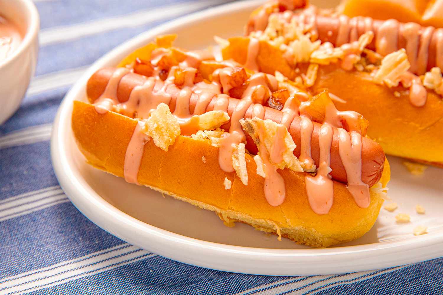 Colombianstyle hot dogs topped with crumbled chips and a pink sauce on a plate