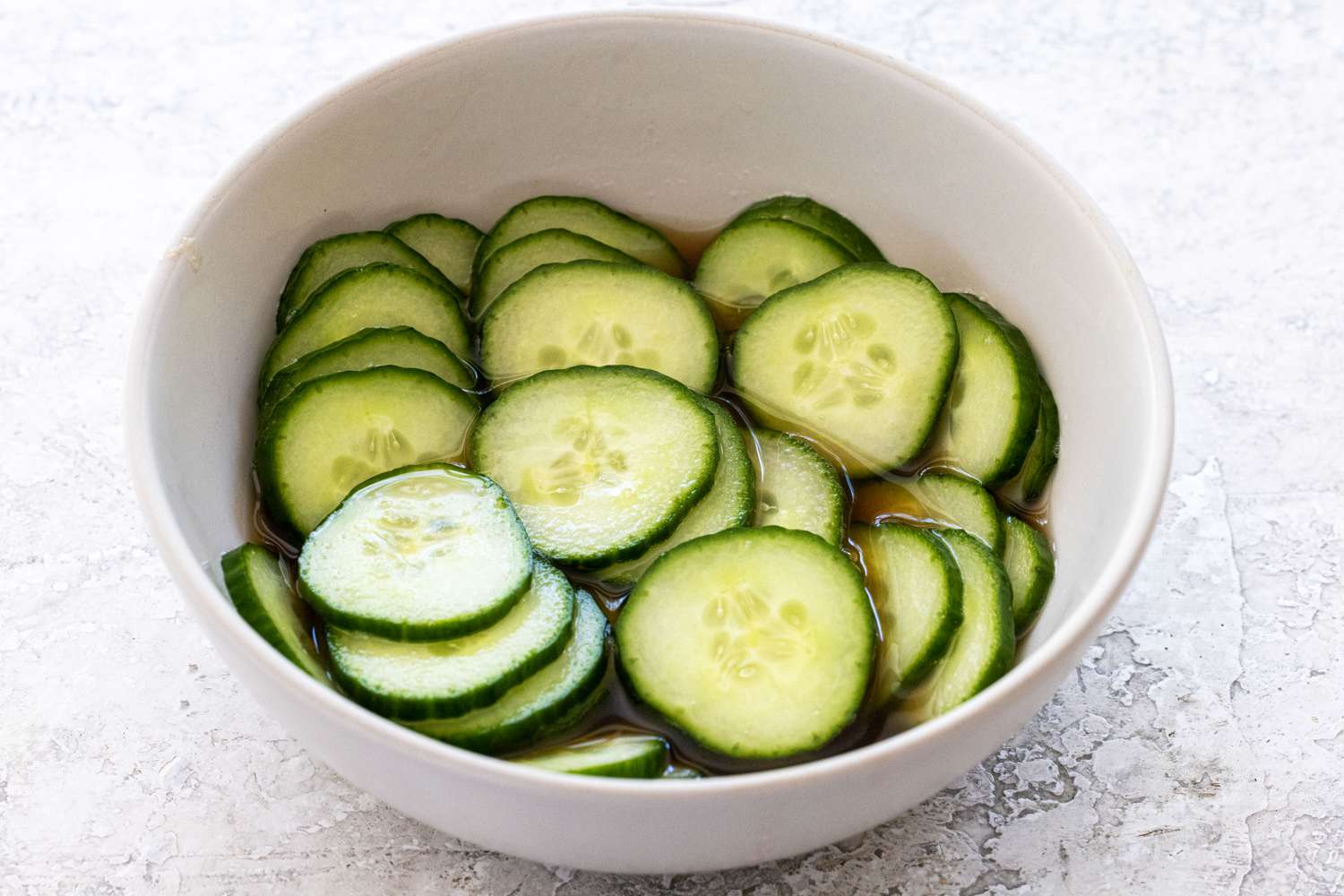 Cucumber slices pickling in a bowl to make smoked salmon, cucumber, and cream cheese crostinis.