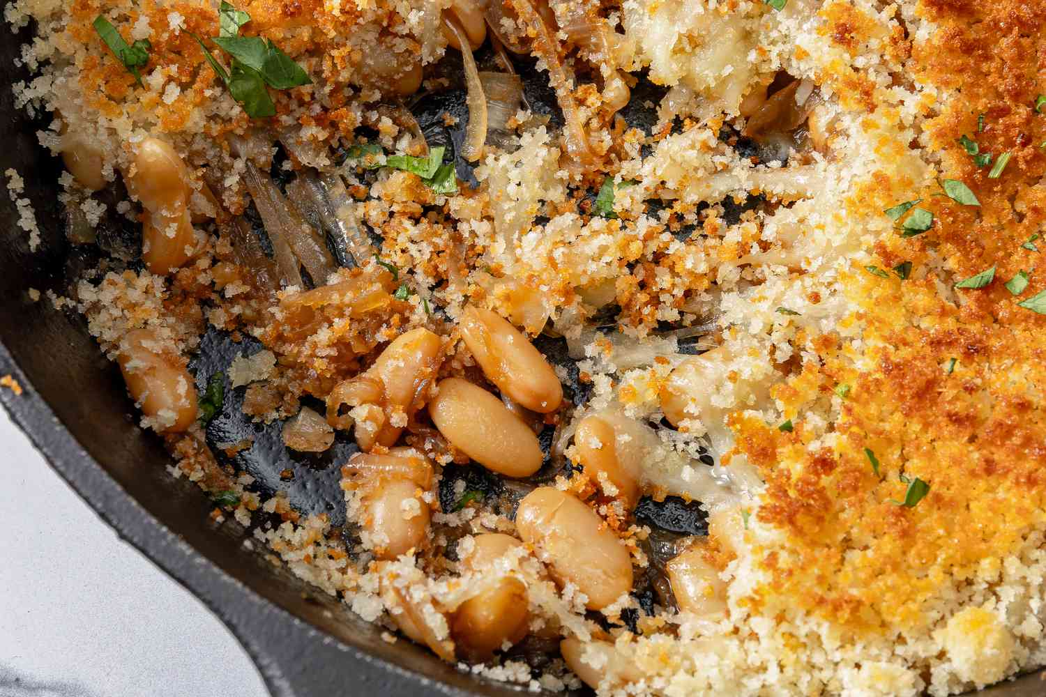 A closeup of baked french onion beans in a cast iron skillet