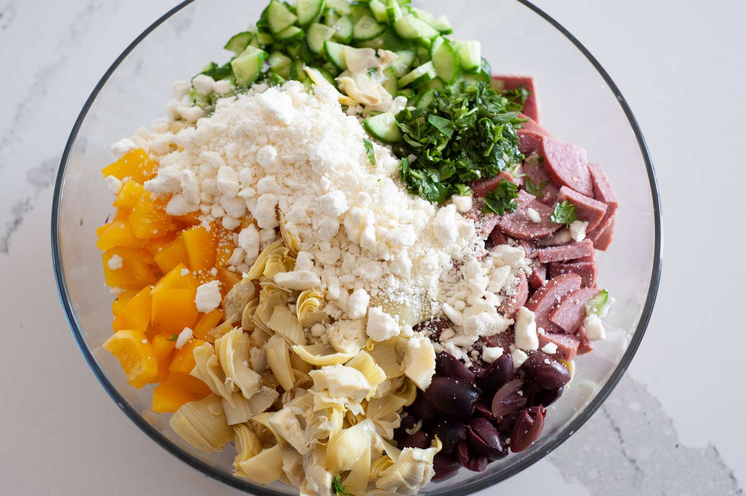 Chopped Ingredients (Bell Peppers, Sausage, Artichoke Hearts, Cucumbers, Cheese, and Olives) in a Bowl for Tortellini Salad