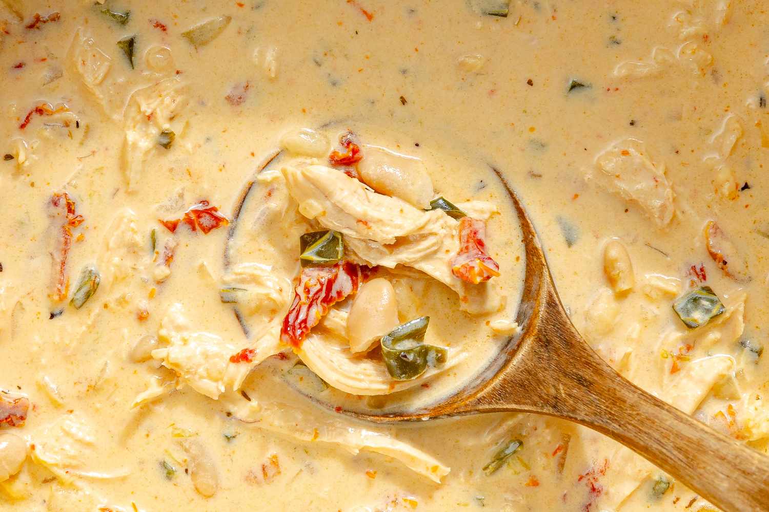A closeup of creamy Marry Me Chicken Chili with a wooden spoon containing shredded chicken beans and vegetables