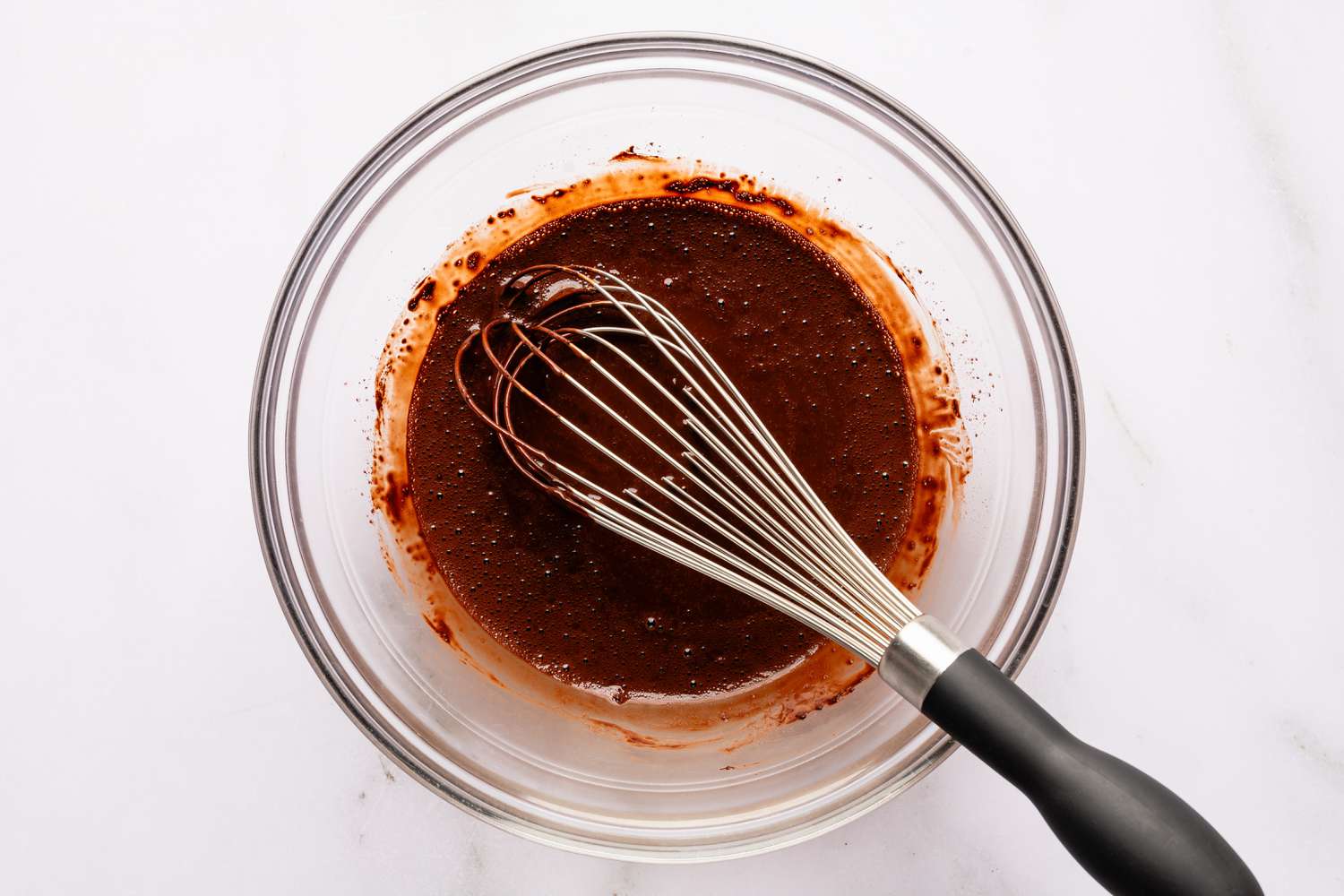Overhead view of a clear glass bowl and whisk with cocoa and hot water after whisking together for Easy Brooklyn Blackout Cake recipe