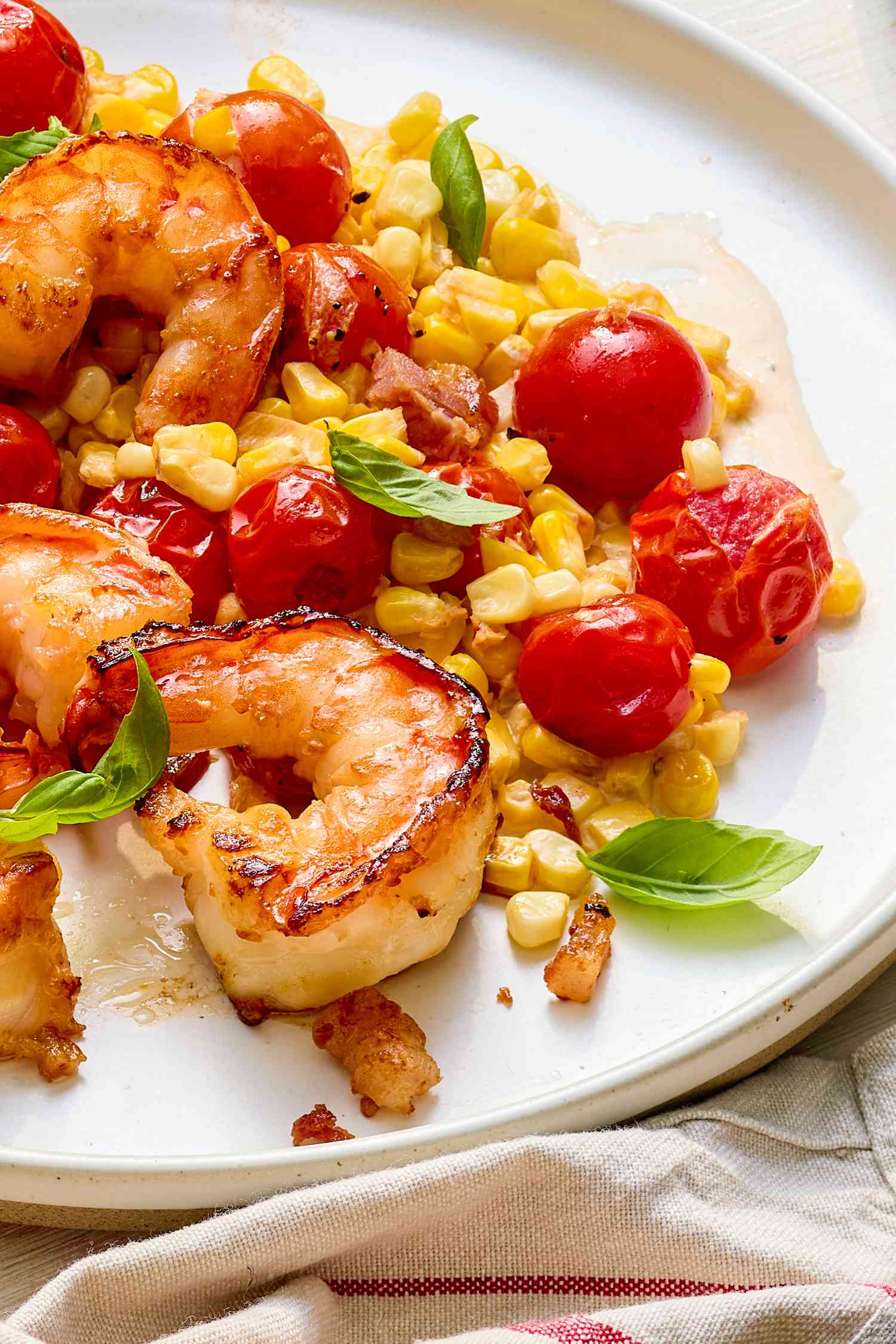 Close-up: plate of creamy skillet shrimp with corn, pancetta, and tomatoes on a white and red table napkin