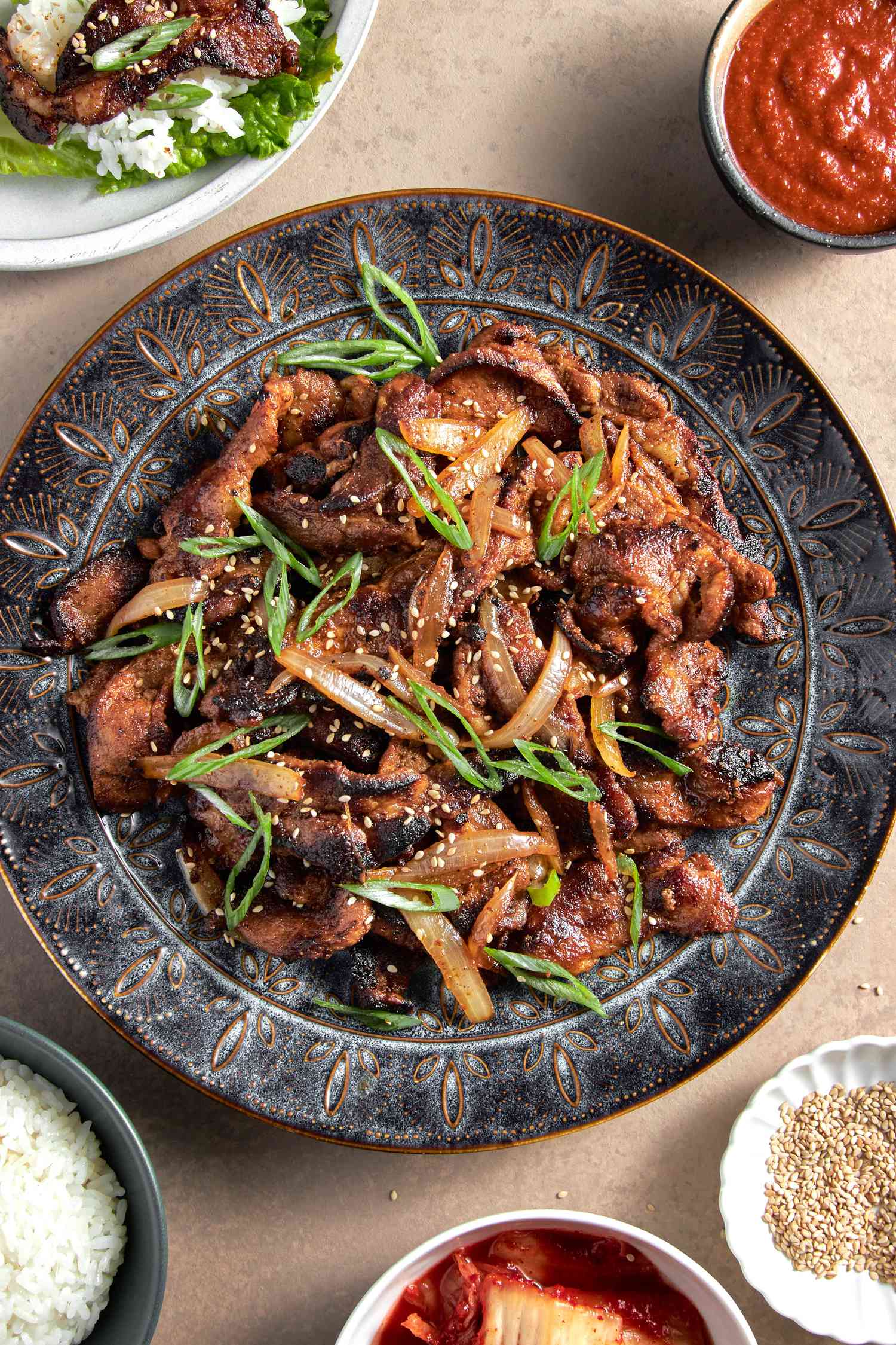 Spicy pork bulgogi on a platter, surrounded by condiment bowls