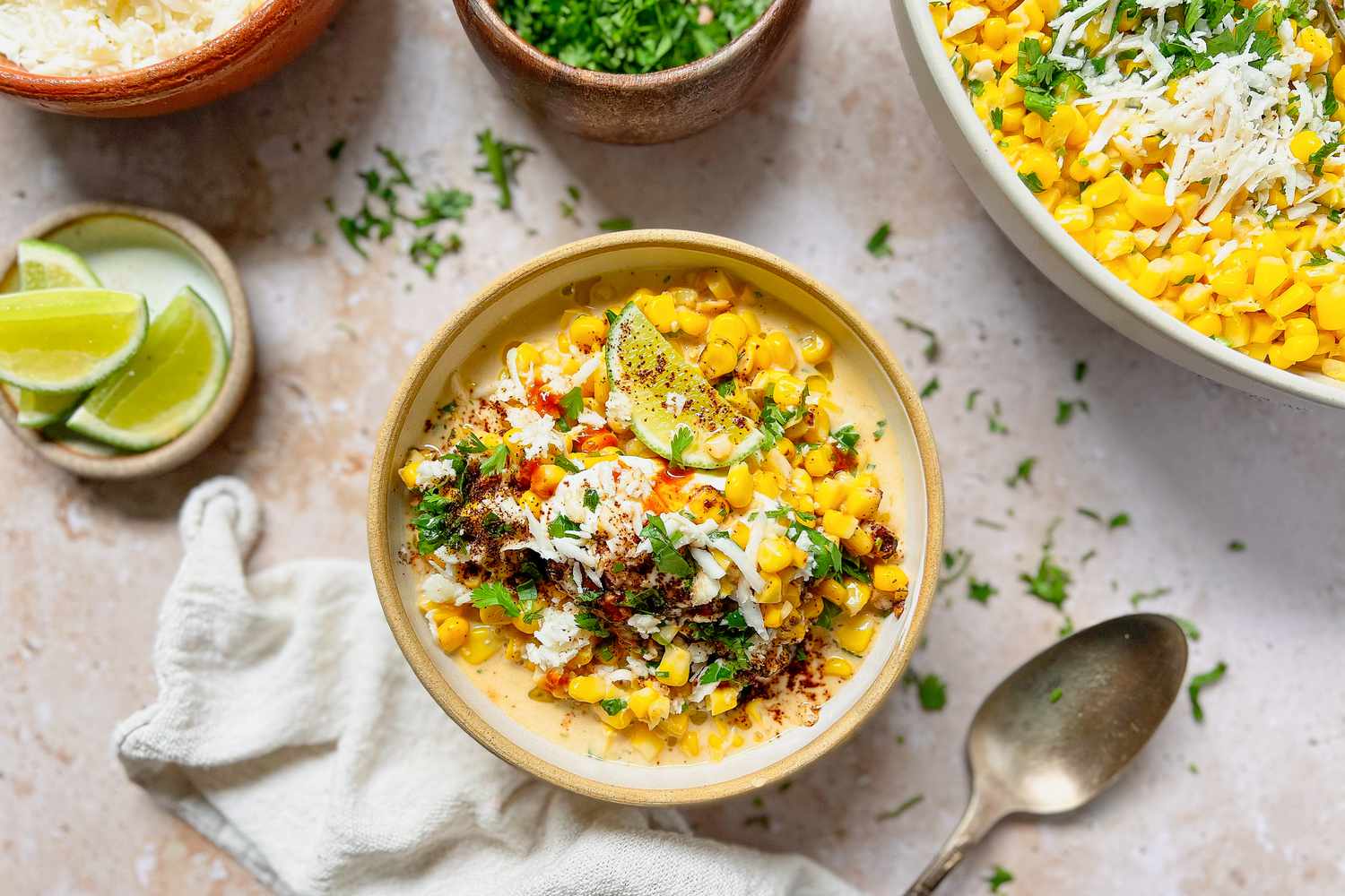 Bowl of Esquites Topped with Cilantro, Cotija Cheese, and Ancho Chile Pepper Surrounded by Bowls of Toppings
