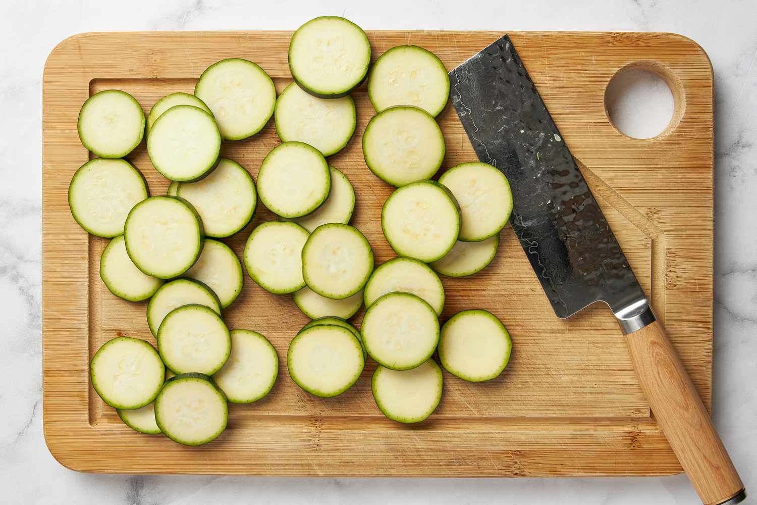Zucchini slices into thin slices on a cutting board with a knife