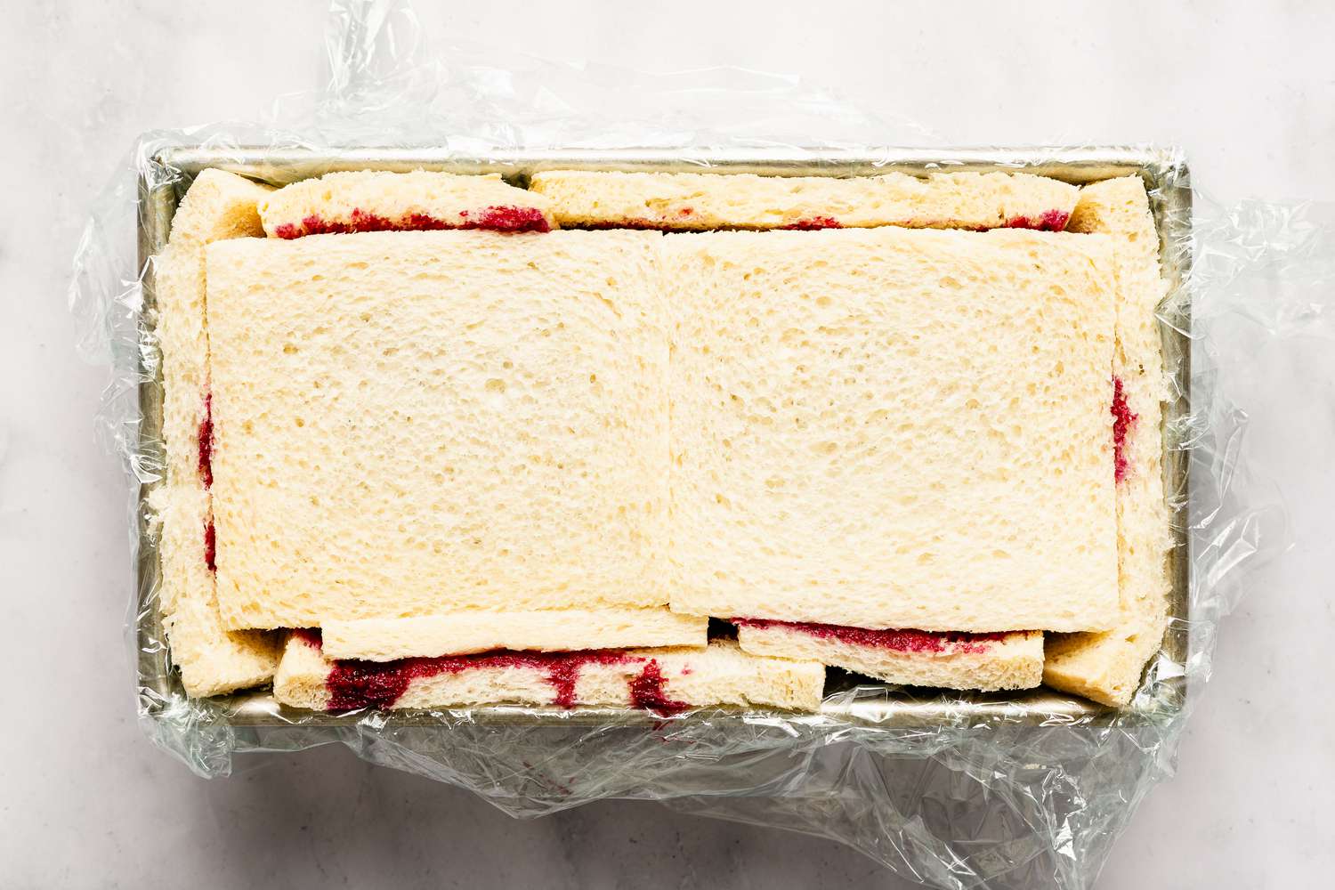 Overhead view of a metal bread baking pan with bread slices lining the top and inside for Easy British Summer Pudding recipe