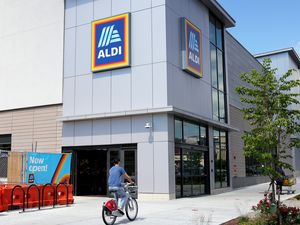 Exterior of an ALDI grocery store with a pedestrian riding a bicycle past the entrance