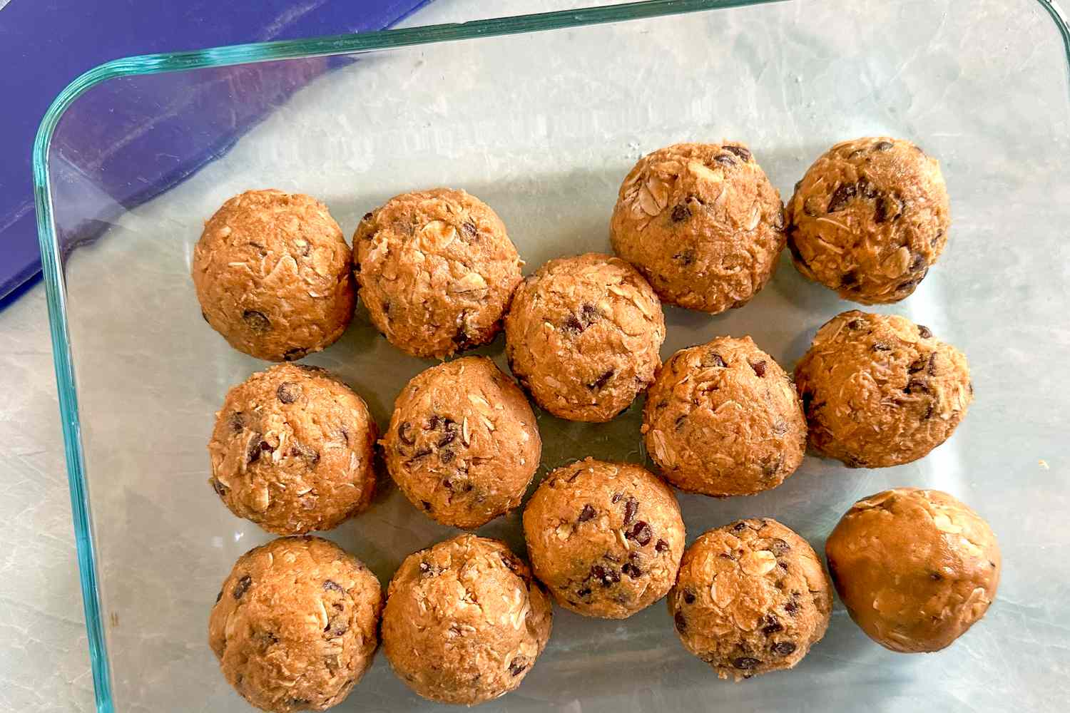 Overhead view of a clear glass bowl of fourteen energy balls on a marble counter