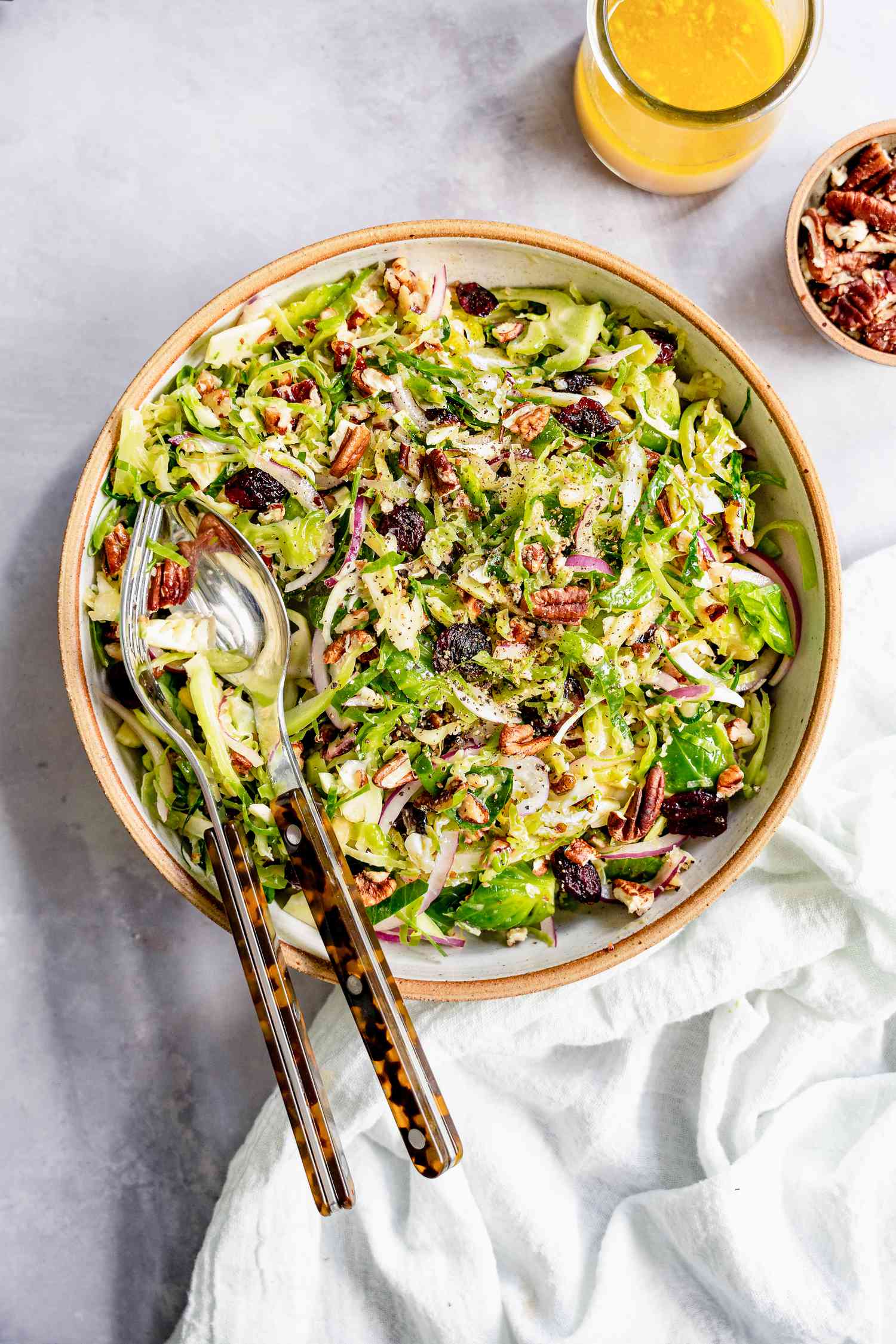 Brussel Sprout Cole Slaw in a Bowl Next to a Bowl of Dressing and Bowl of Pecans