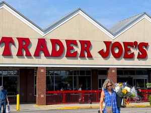 A Trader Joes storefront with a person holding flowers walking in the foreground