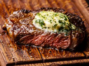 A grilled steak topped with herb butter on a wooden surface