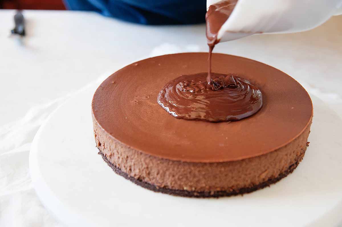 Pouring chocolate ganache over the top of the best chocolate cheesecake
