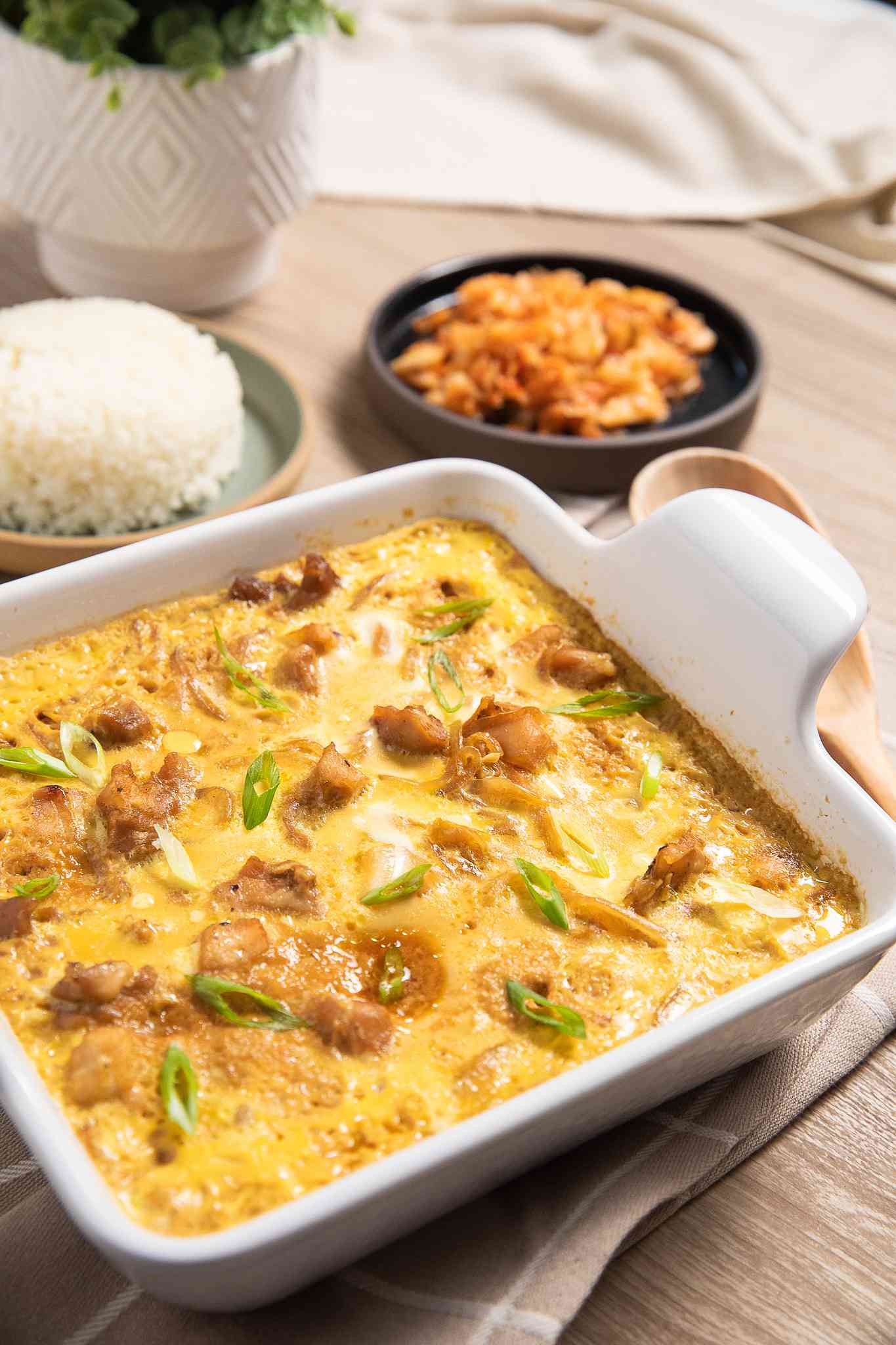 Microwave Oyakodon (Japanese Chicken and Egg Rice Bowl) in a Microwavable Dish, and in the Background, a Small Plate With Cooked Rice and a Small Plate of Kimchi