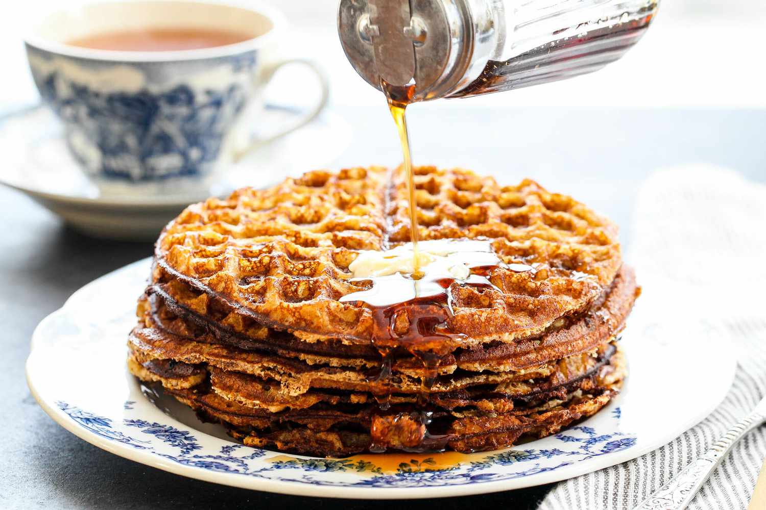 A stack of almond flour waffles on a plate as syrup is poured on top