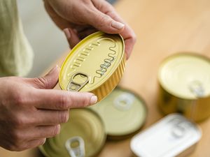 Person inspecting a sealed food can with other cans nearby on a wooden surface