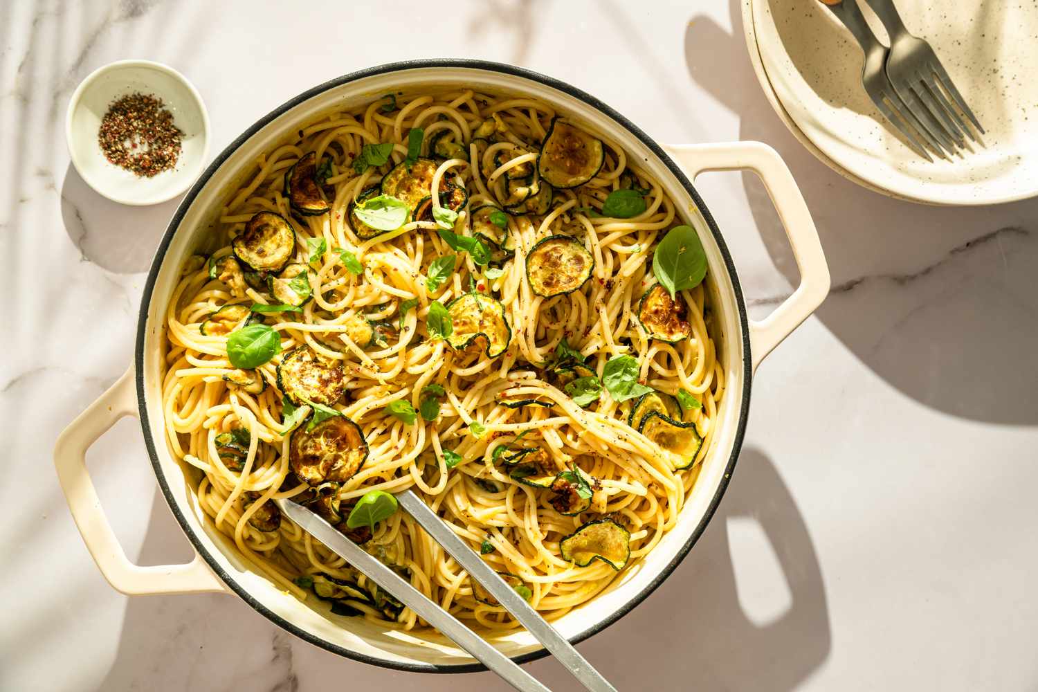 Spaghetti with zucchini and herbs served in a pot, with utensils on the side