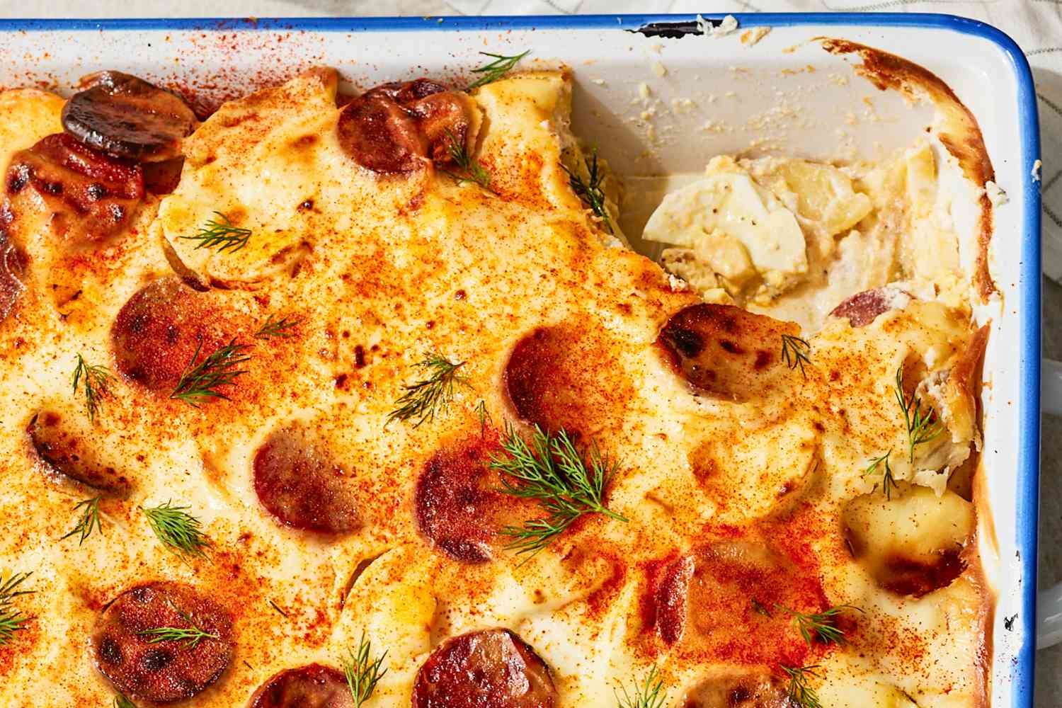 close up of Rakott Krumpli (Hungarian Potato Casserole) in a 9x13 casserole dish, one serving scooped out.