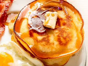 A plate with pancakes topped with butter and syrup served alongside bacon and a fried egg